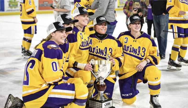 女子冰球队的队员戴着冠军帽，拿着奖杯在冰上摆姿势